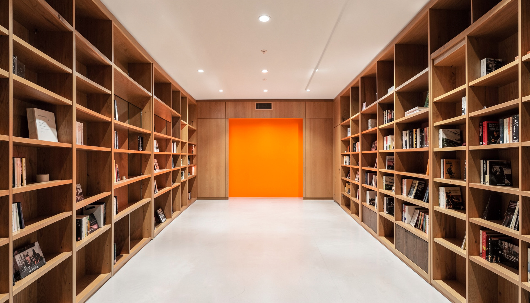 A clean architectural photograph of a modern music library interior with symmetrical shelving, warm wood tones, and soft overhead lighting, calm and orderly