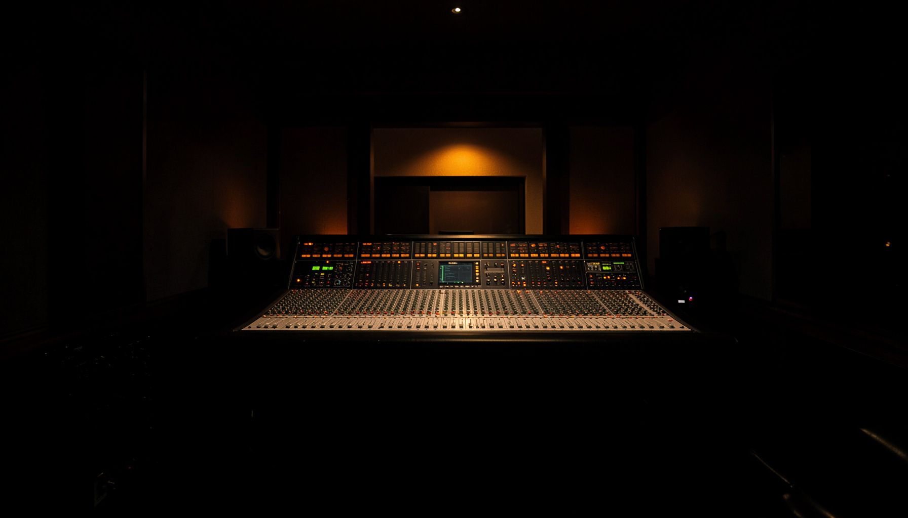 A dark atmospheric photograph of a recording studio control room with mixing console, warm amber accent lights glowing against deep black equipment, moody and professional
