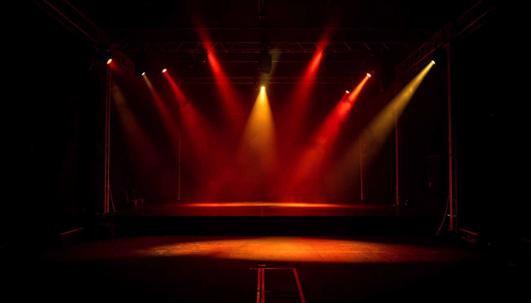 A dark atmospheric wide shot of concert stage lighting in deep red and gold, empty stage with dramatic spotlights, moody and powerful