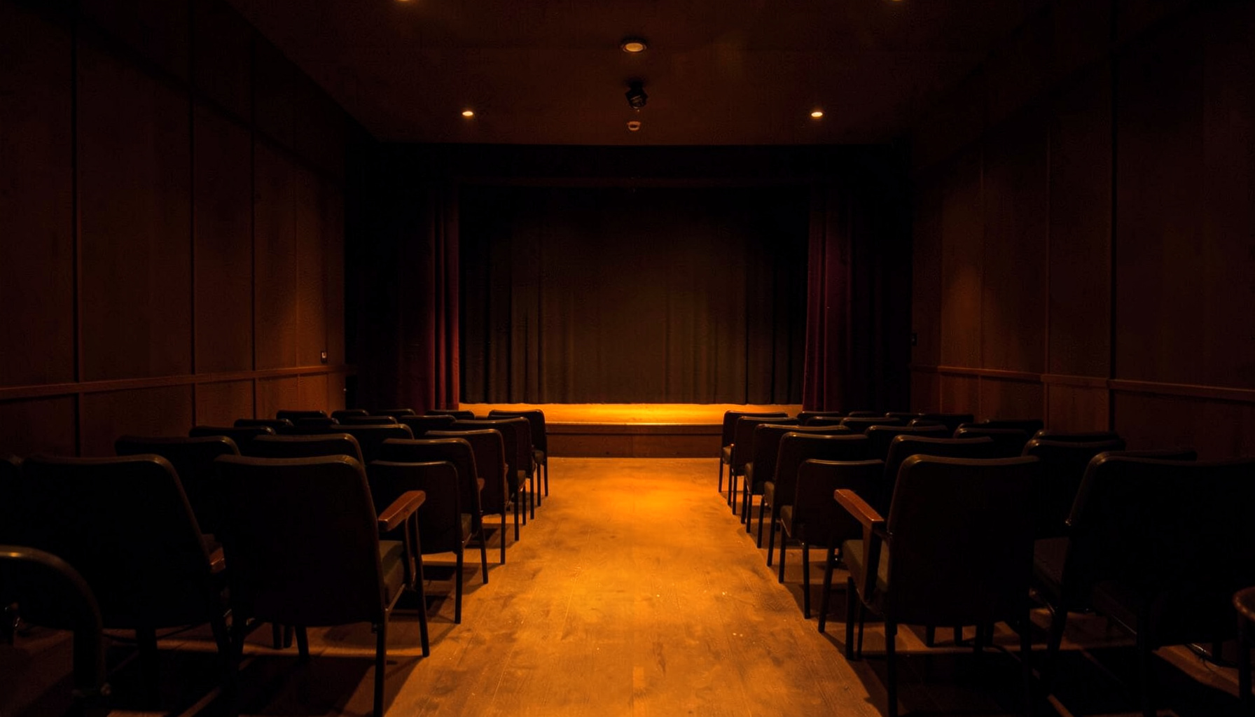A quiet, dim jazz club interior in warm amber and deep brown tones, with a symmetrical row of empty chairs facing a small stage, evoking a calm, reflective mood
